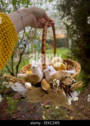 Hand holding rustic easter basket with eggs and treats outdoors Stock Photo