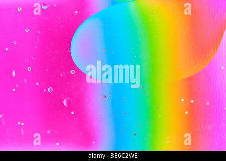 Large teal oil drop floating amidst small droplets over bright pink and rainbow colored liquid Stock Photo