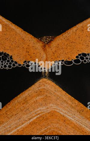 Golden sand flows down through bubbles, forming perfect symmetrical pyramid on black background Stock Photo
