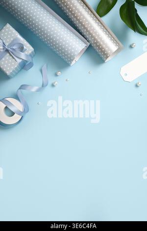 Gift wrapping with blue and silver wrapping paper, ribbon, scissors, and small gift boxes on blue backdrop. Copy space. Stock Photo
