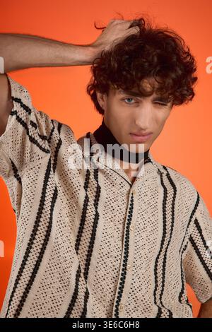 Curly haired man showcases his style in trendy clothes against an orange backdrop. Stock Photo