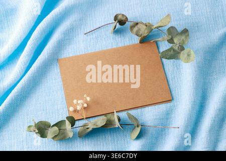 Vintage brown blank paper card and aroma dried eucalyptus twigs on blue linen background. Floral mockup postcard with copy space Stock Photo
