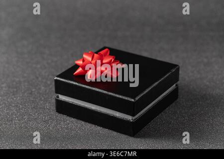 Black gift box with red bow on blurred dark silver glitter background. Celebration greeting or black Friday  card mockup with copy space Stock Photo