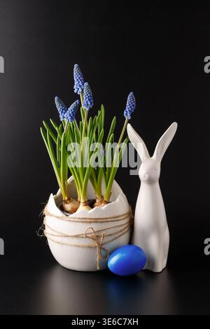 Happy easter decoration on black background. Blue muscari flowers in ceramic white pot, rabbit figure  and painted egg as interior decor. Easter card Stock Photo