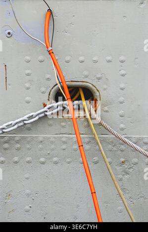 Close-up view of grey ship's hull, with rivets, heavy chains, cables, and textured metal surface Stock Photo