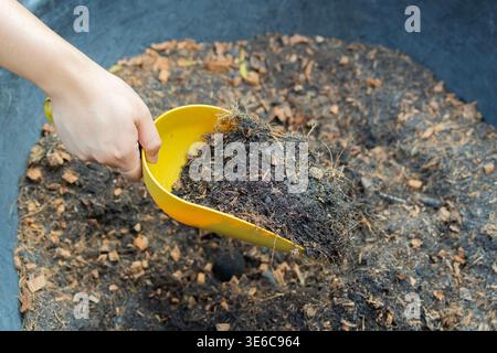 Close-up of a gardener's hand using a small trowel to cultivate rich, dark soil in a garden, preparing for planting during the spring season Stock Photo