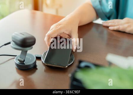 Woman placed smartphone on a wireless charger next to an earphones charging on wireless pad at work space. Technology, multiple sharing and lifestyle Stock Photo