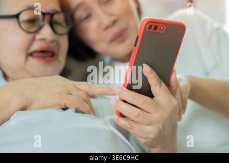 Happy family concept. Eldely mother and daughter use the phone on the livingroom at home. They laugh and have fun. Selective focus. Mother Day Concept Stock Photo