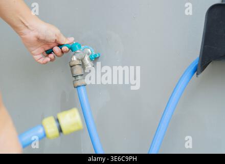 Selective focus and Close-up of a woman hand opening hose faucet at home a sunny day.  Hand turn on or turn off faucet Stock Photo