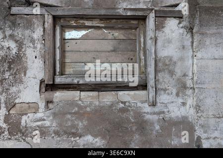 Old dirty brick wall with cement plaster and sealed wooden window on damaged house. Destroyed house wall texture. Stock Photo