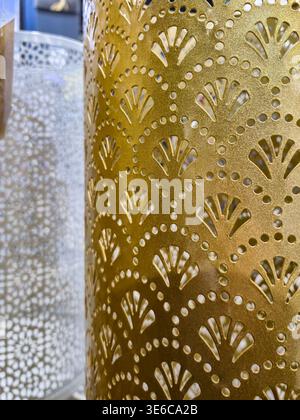 A detailed view of a metallic gold lantern featuring a repeating fan-shaped pattern and small perforations, with another decorative object softly visi Stock Photo