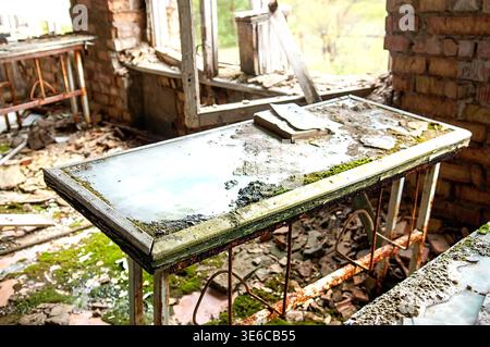 Ukraine, Pripyat : Decaying glass-top metal lab table covered in moss and water puddles with old book and debris inside derelict school classroom feat Stock Photo