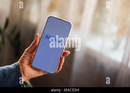 Hand of a person holds a smartphone showing the text "AI agent," with a soft-focus background of curtains and indoor plants in a cozy interior Stock Photo