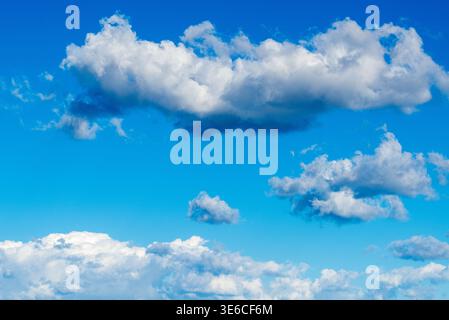 Bright blue sky is filled with soft cumulus cloud shapes, including a long dense cloud band and scattered smaller puffs in the distance. Stock Photo