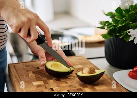 Process of woman cutting avocado for toasts in kitchen interior. Woman preparing healthy breakfast at morning. Vegan food Stock Photo