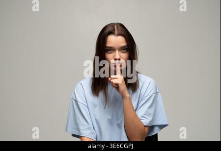 Young woman making a shush gesture, asking for quiet or keeping a secret. Serious expression, finger on lips Stock Photo
