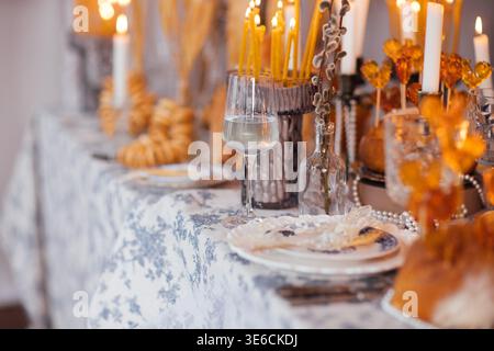 Dining table beautifully arranged with golden candles, decorative items, and a glass of water, creating an inviting setting for a festive meal, Easter Stock Photo