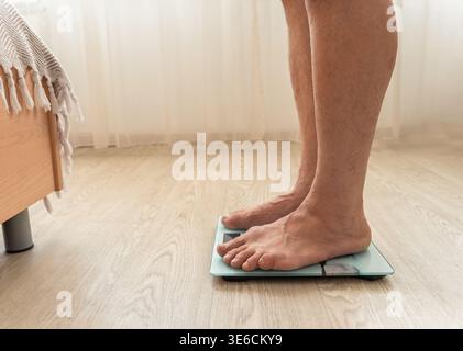 Man standing barefoot on a digital weight scale, checking his weight in the morning as part of a health and diet routine Stock Photo