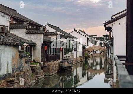 Historic Chinese water town architecture frames a tranquil canal with a classic stone bridge under a soft morning sky Stock Photo