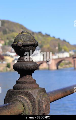 Ornate rusty iron railing post with the historic Old Bridge (Alte Brücke) and Neckar river in the background, Heidelberg, Germany. Stock Photo