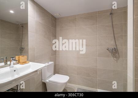 Modern bathroom with beige tiles, a white toilet, and a sink. Natural light illuminates the space, creating a clean and minimalist atmosphere. Stock Photo