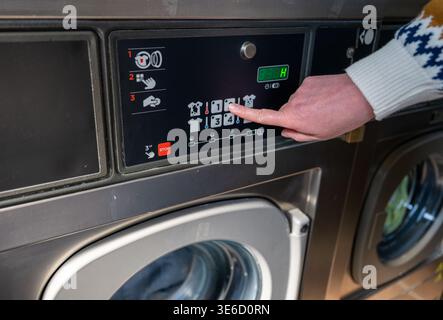 Close up of hand selecting washing program on modern laundromat machine control panel Stock Photo