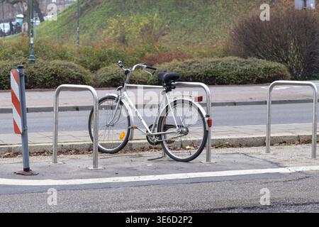 Silver bicycle with black seat securely locked to a public metal rack on a city sidewalk, symbolizing sustainable urban mobility and eco-friendly dail Stock Photo