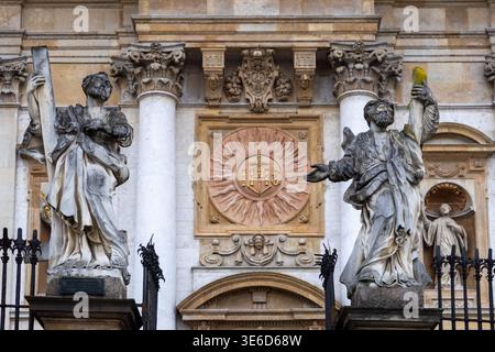 Krakow, Poland - December 2, 2025: Grand Baroque church facade featuring weathered stone statues of saints, classical columns, ornate IHS monogram, sy Stock Photo