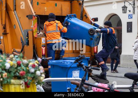 Krakow, Poland - December 2, 2025: Two TMPQ sanitation workers in reflective gear efficiently empty blue recycling bins into a large orange truck at G Stock Photo