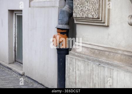 Detail of a rustic orange and black downspout on a concrete building, depicting urban utility, texture, and the unique aesthetic of old city structure Stock Photo