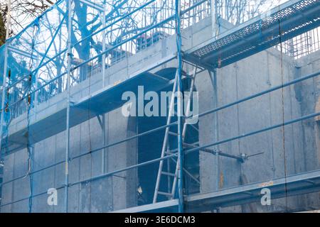 Detailed view of a protective blue safety net draped over metal scaffolding, surrounding a new concrete building with an arched opening, signifying on Stock Photo