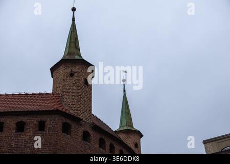 Krakow, Poland - December 1, 2025: Low-angle shot of ancient brick fortress towers with pointed green spires under a cloudy sky, conveying European me Stock Photo