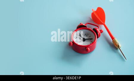 Red alarm clock and red dart isolated on blue background representing urgent deadlines and targeting. Stock Photo