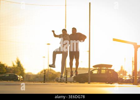Athletic couple jumping high on an outdoor court during a bright sunset Stock Photo
