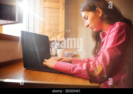 Woman with long dark hair types on laptop at wooden desk, sunlight illuminating the scene, with a coffee cup and stationery in the background Stock Photo