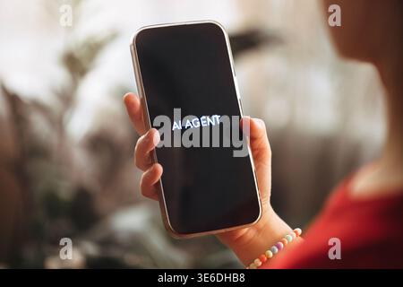 Individual holds a smartphone showing the text "AI AGENT" against a softly blurred indoor setting with greenery in the background Stock Photo