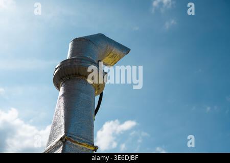 Industrial metal ventilation pipe or exhaust chimney with insulation wrap against a blue sky with clouds. Copy space Stock Photo