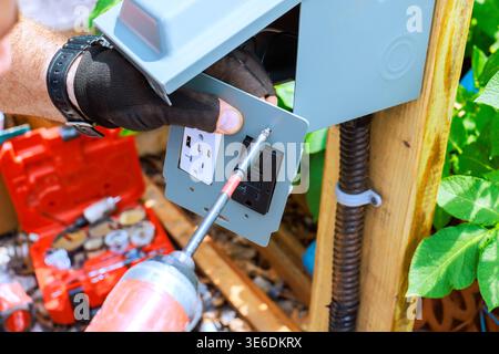 Contractor is working on installing an outdoor electrical outlet in wooden post at garden. Stock Photo