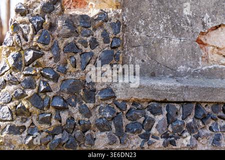 Detailed texture of an old wall featuring dark jagged stones embedded in grey concrete and weathered plaster surfaces. Stock Photo
