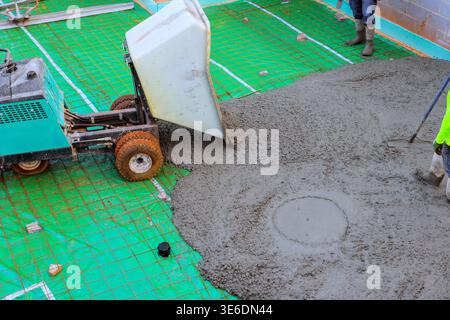 Two workers prepare spread concrete on construction site using wheelbarrow bucket Stock Photo