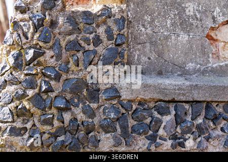 Detailed texture of an old wall featuring dark jagged stones embedded in grey concrete and weathered plaster surfaces. Stock Photo