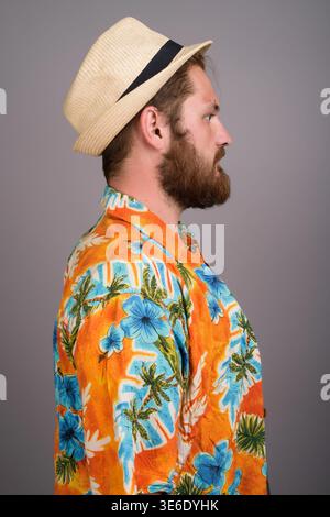 Side profile of a young Caucasian man with a beard wearing a vibrant orange floral Hawaiian shirt and trilby straw hat. Ideal for travel, vacation, an Stock Photo