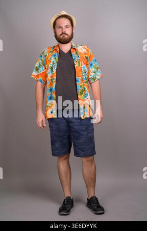 Full length studio shot of a young Caucasian man with a beard wearing a vibrant orange floral aloha shirt, blue shorts, and a trilby hat. Perfect for Stock Photo