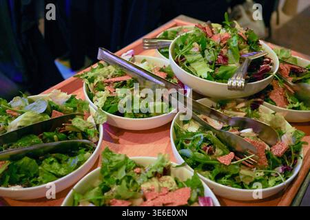 Rows of fresh arugula and radicchio salads topped with crunchy sesame crisps in white bowls on a catering tray, ideal for professional event. Stock Photo