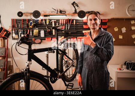 Smiling young bicycle mechanic repairing broken bike showing on copy space with finger in the repair shop. copy space Stock Photo