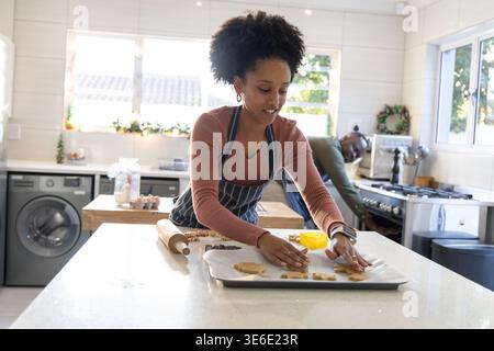 Couple baking, woman arranging cookie dough on parchment tray using yellow cutter, washing machine Stock Photo