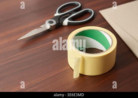 roll of yellow masking tape and black scissors on table top surface, top view with copy space, craft and office background Stock Photo