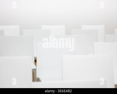 Rows of empty white chairs filling a clean, modern, and minimalist interior space Stock Photo