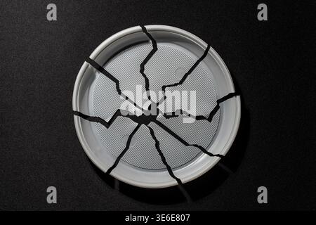 Top view of cracked white plastic plate on black background symbolizing damage fragility waste and environmental pollution concept, close up Stock Photo