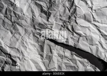 Dramatic texture of wrinkled white paper with a diagonal tear showing dark space. Grungy minimalist background with sharp shadows and paper edges. Tor Stock Photo